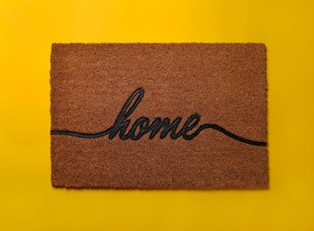 Doormat with word Home on yellow background, top view