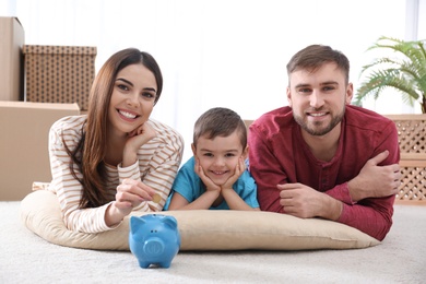 Photo of Happy family with piggy bank and money on floor at home