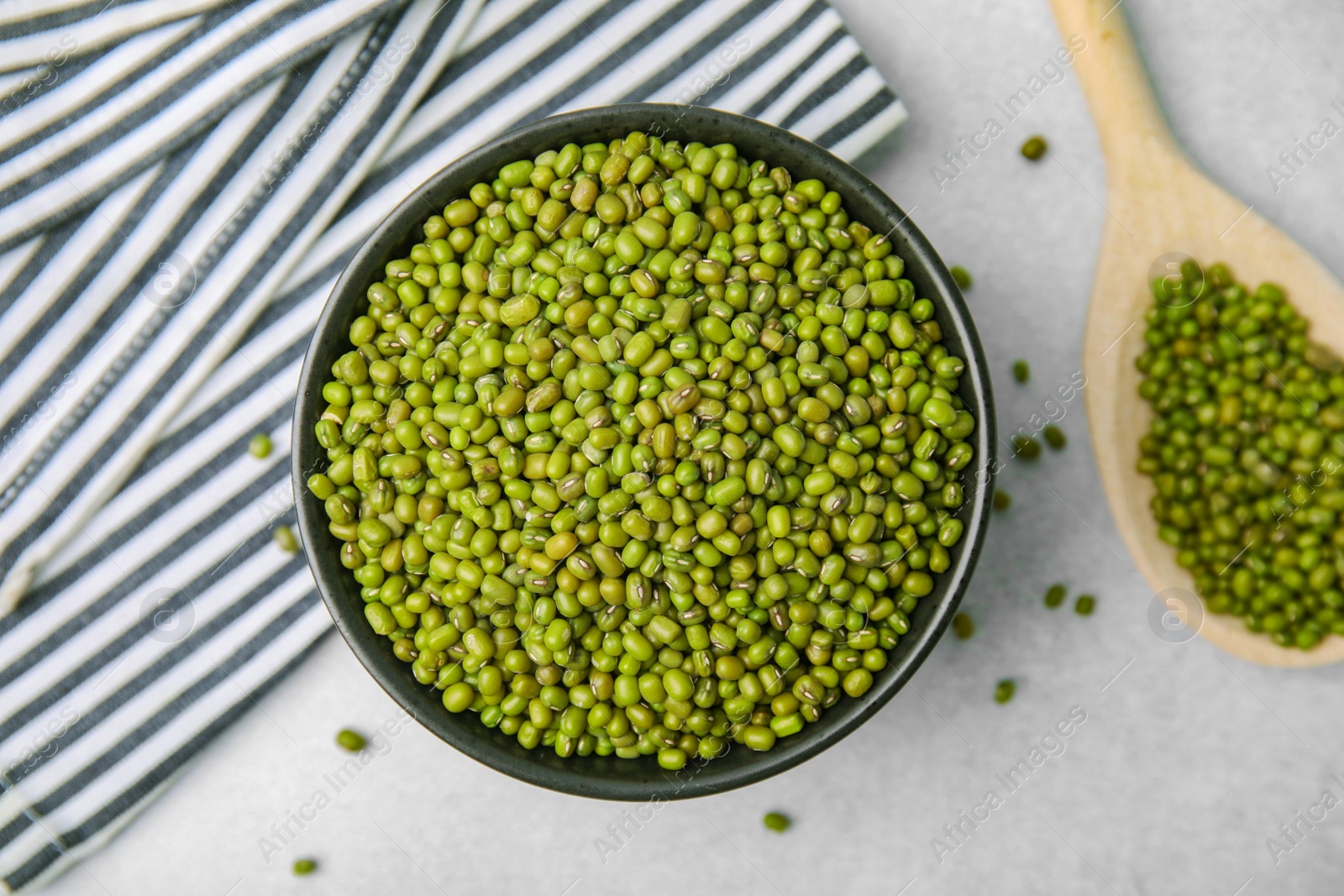 Photo of Bowl and wooden spoon with green mung beans on light grey table, flat lay