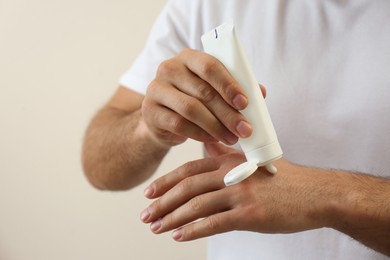 Photo of Man applying cream from tube onto hand on beige background, closeup