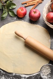 Photo of Fresh dough, rolling pin, ingredients and leaves on grey table. Making apple pie