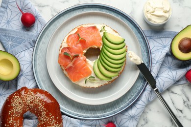 Photo of Delicious bagel with cream cheese, salmon and avocado on white marble table, flat lay