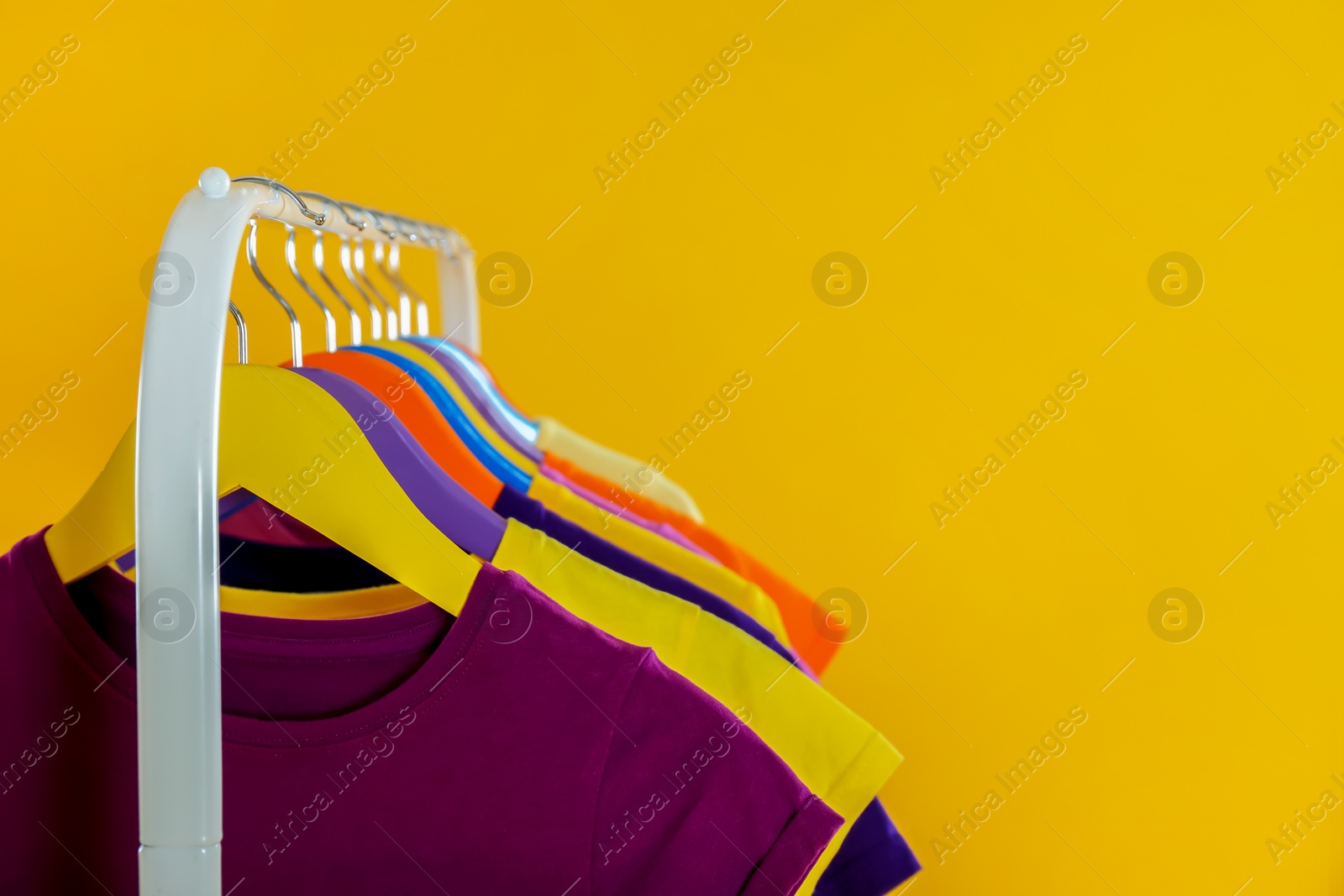 Photo of Rack with stylish children clothes on yellow background, closeup. Space for text