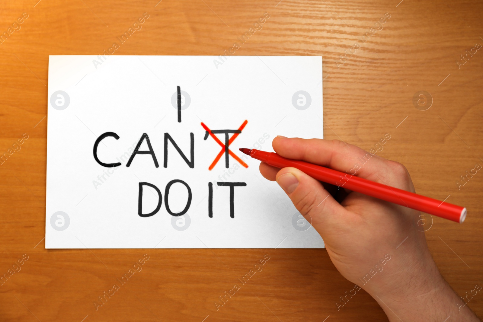 Photo of Man crossing letter T with red felt tip pen making phrase I Can Do It at wooden table, top view