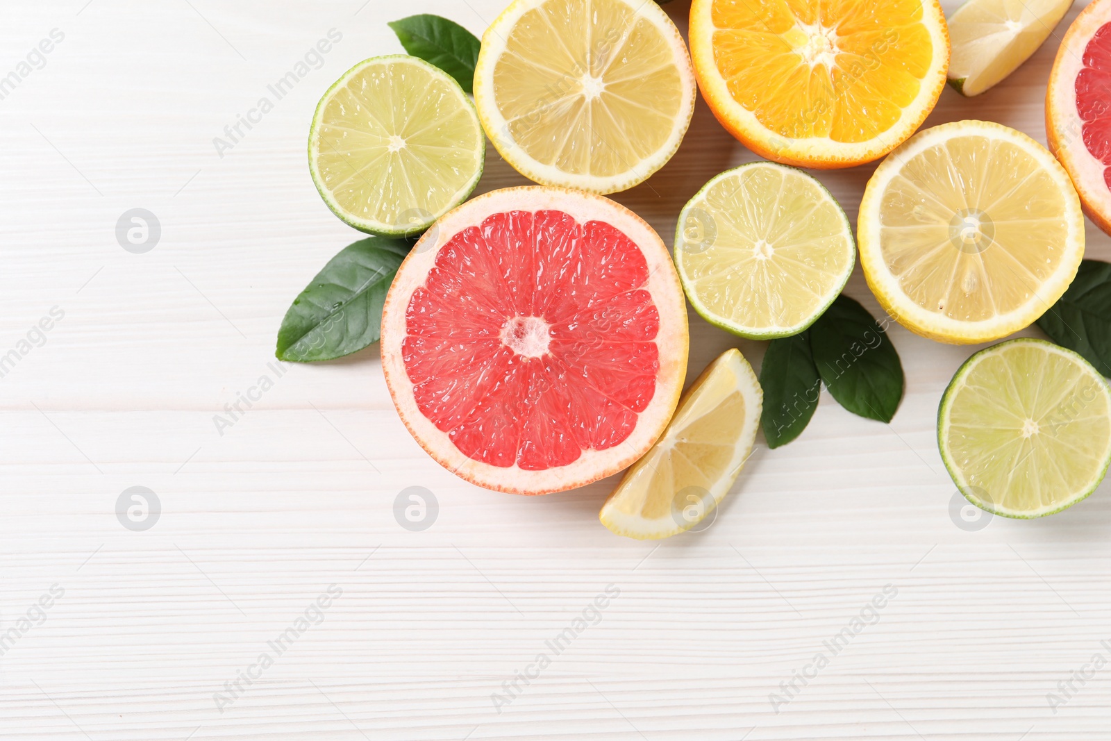 Photo of Different cut citrus fruits and leaves on white wooden table, flat lay. Space for text