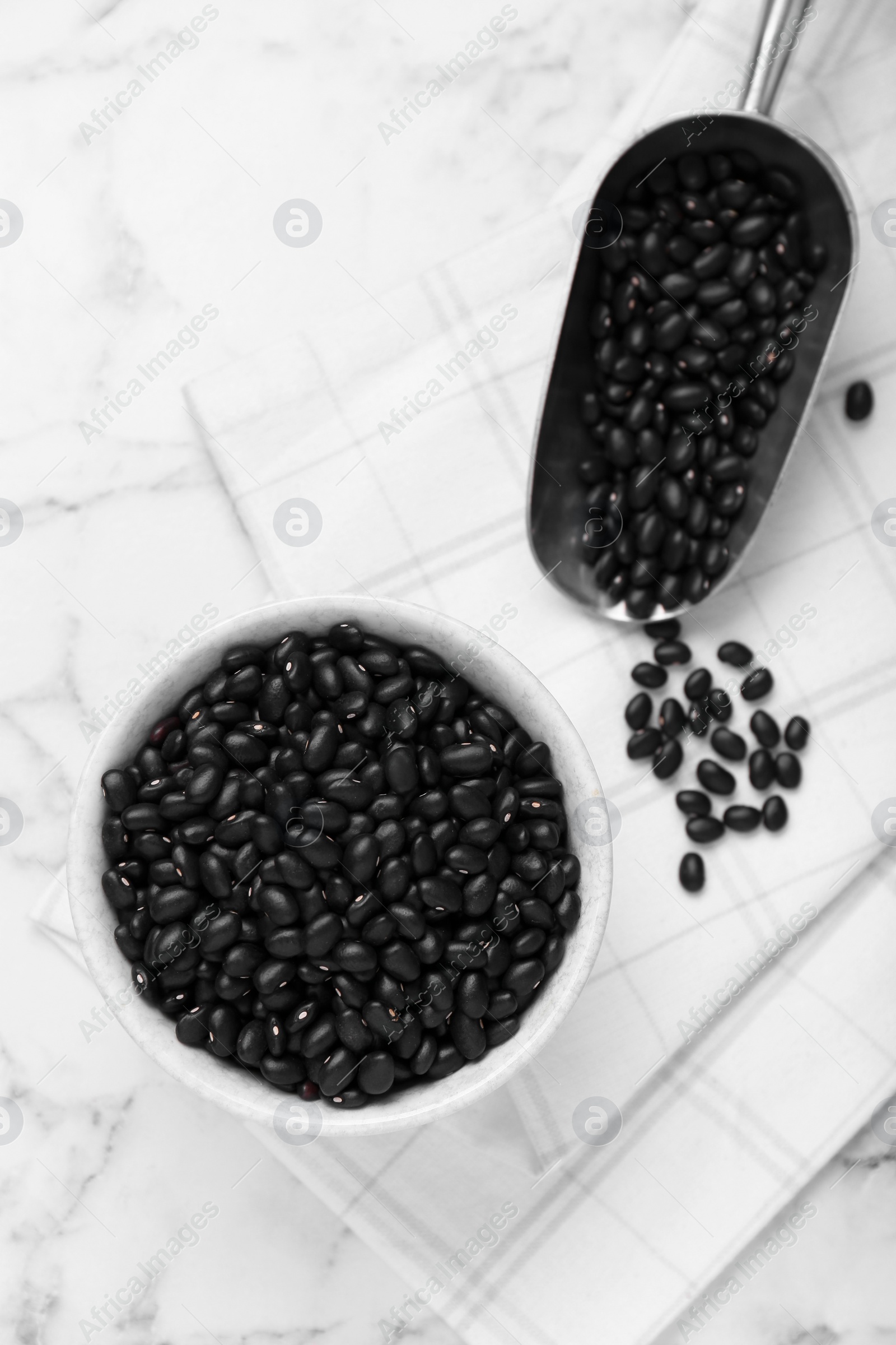 Photo of Bowl and scoop of raw black beans on white marble table, flat lay