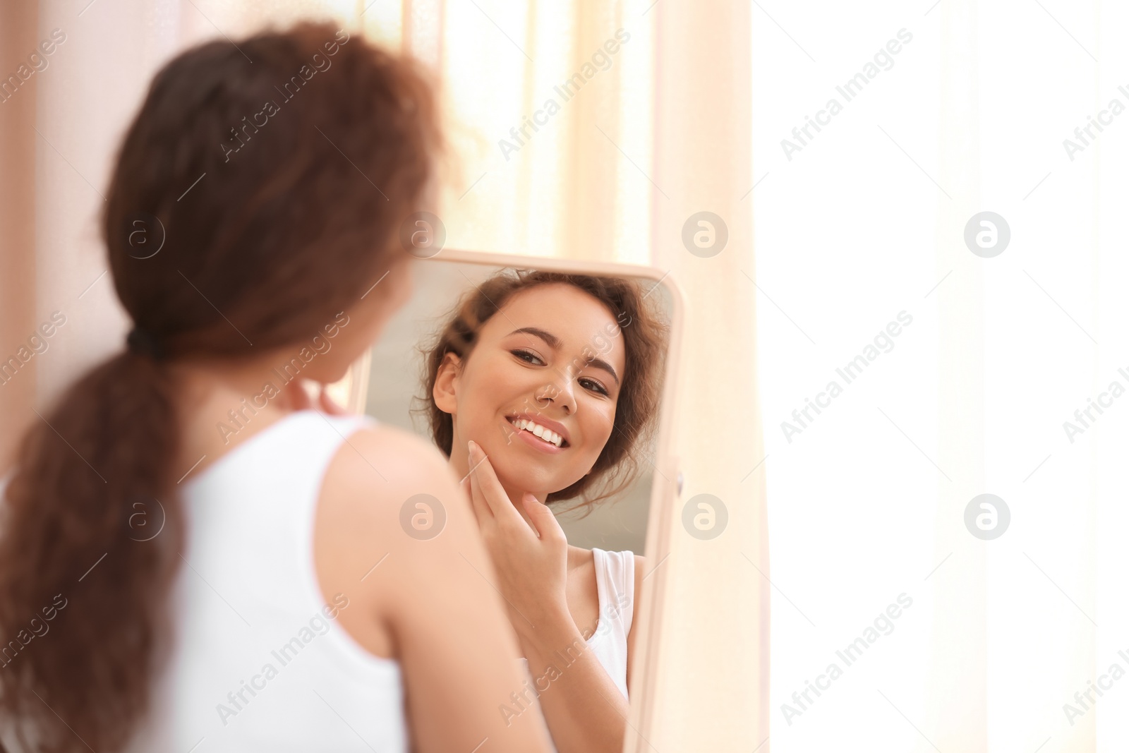 Photo of Beautiful young woman with acne problem looking in mirror at home