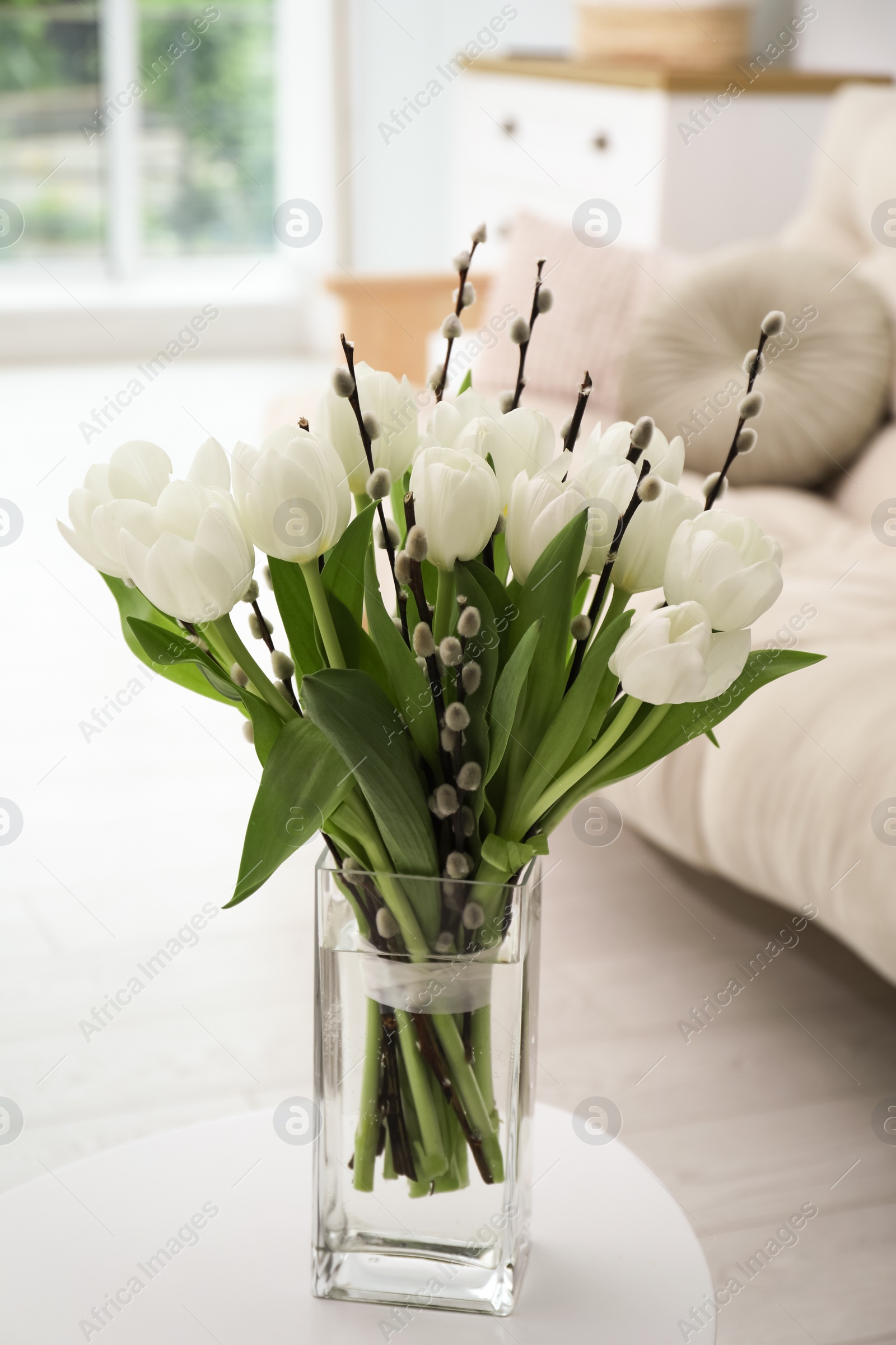 Photo of Beautiful bouquet of willow branches and tulips in vase on table indoors