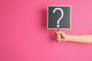 Woman holding blackboard with question mark on pink background, closeup. Space for text