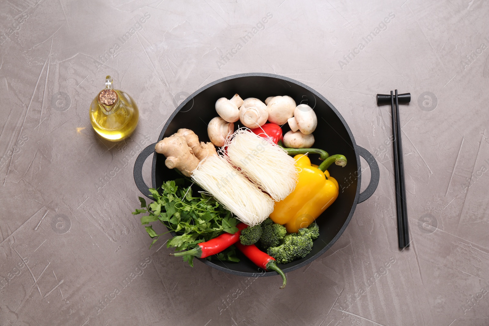 Photo of Wok, chopsticks and different products on grey textured table, flat lay