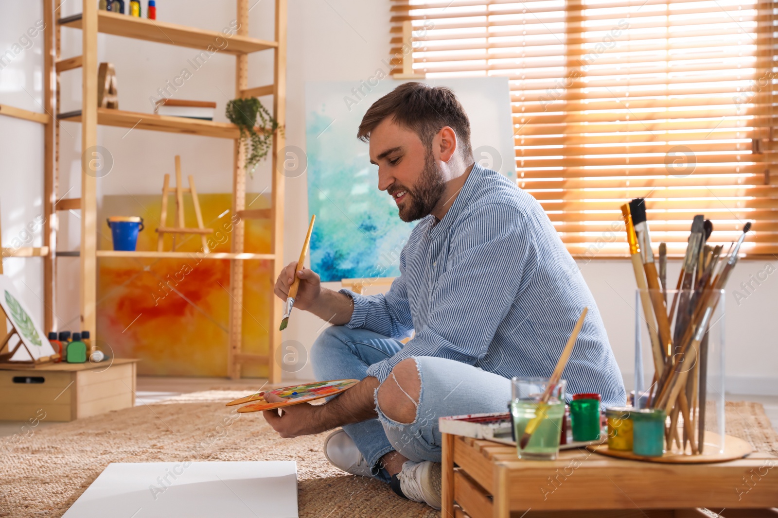 Photo of Young man painting with brush in artist studio