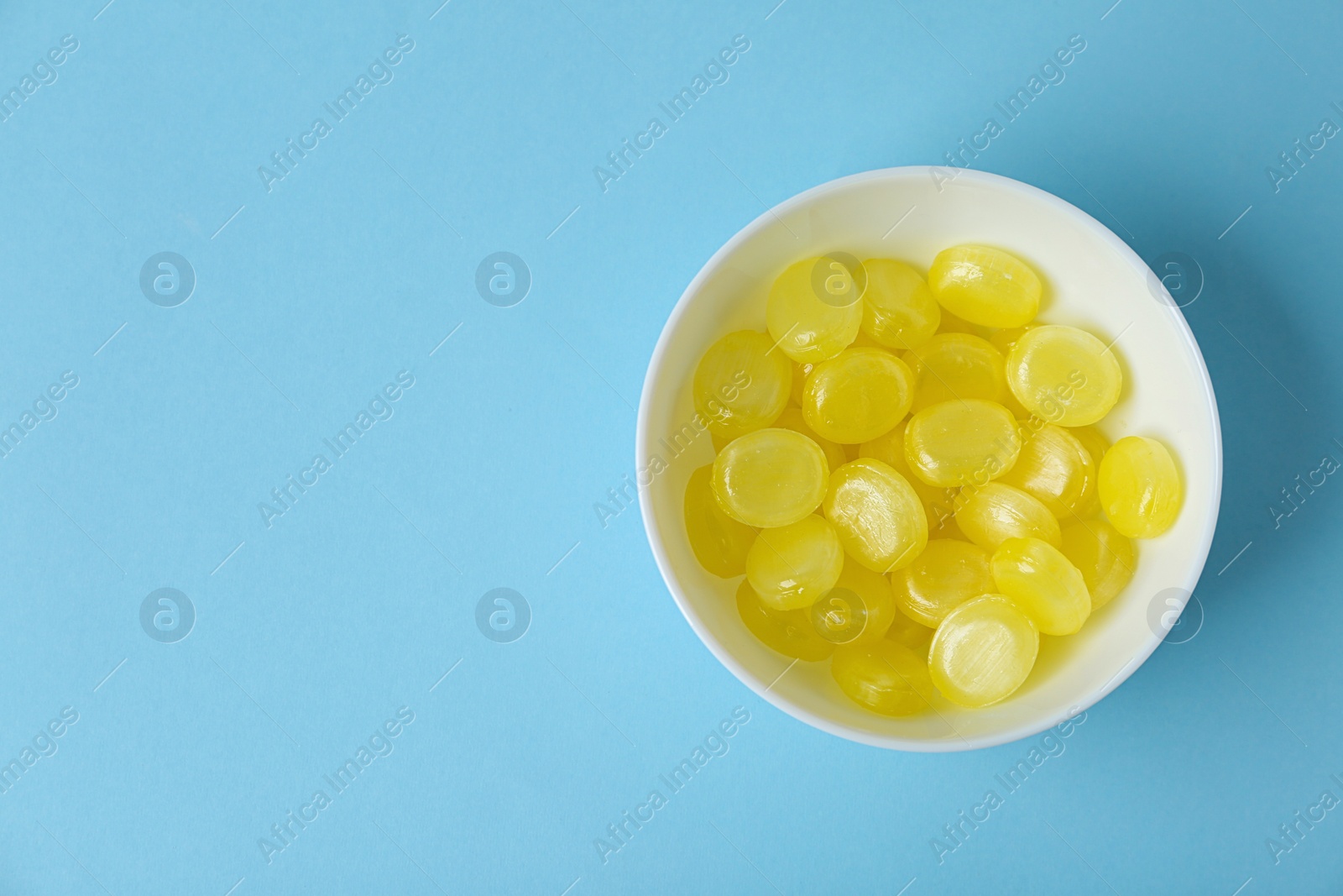 Photo of Delicious lemon drops in bowl on light blue background, top view. Space for text