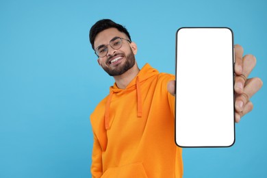Image of Happy man holding smartphone with empty screen on light blue background, space for text