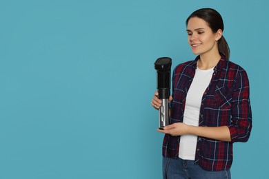 Photo of Beautiful young woman holding sous vide cooker on light blue background. Space for text