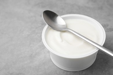 Photo of Delicious natural yogurt in plastic cup and spoon on grey table, closeup. Space for text