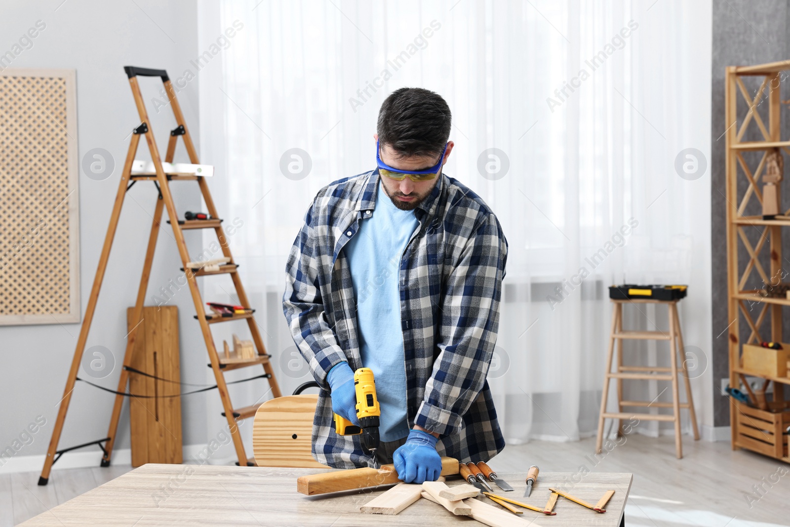 Photo of Young handyman working with electric drill at table in workshop