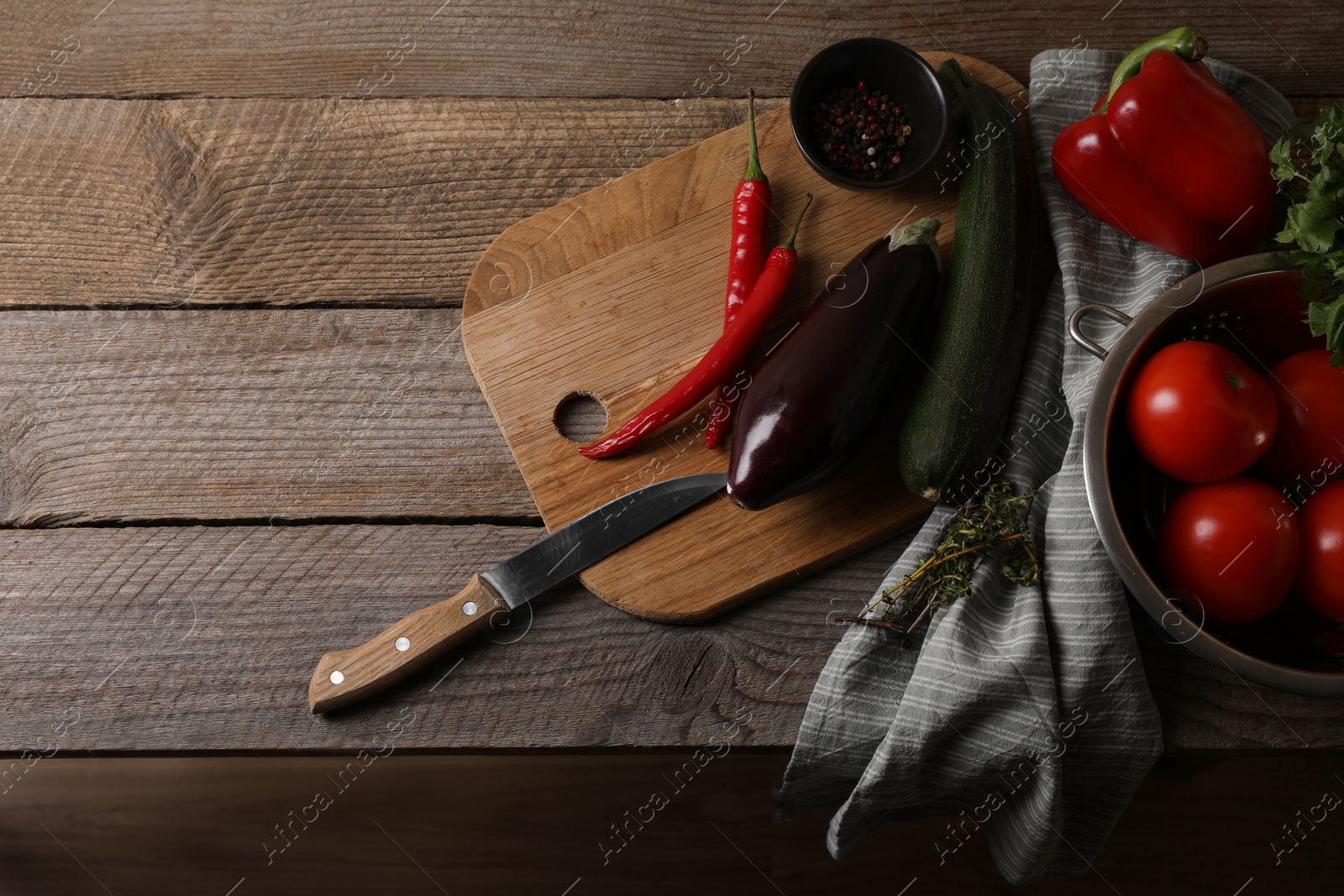 Photo of Cooking ratatouille. Vegetables, peppercorns, herbs and knife on wooden table, flat lay with space for text