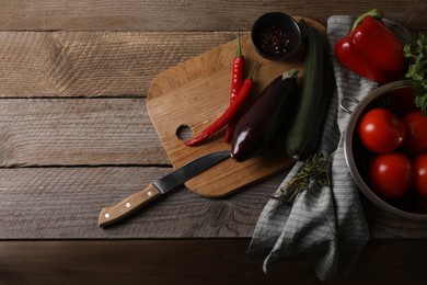 Photo of Cooking ratatouille. Vegetables, peppercorns, herbs and knife on wooden table, flat lay with space for text