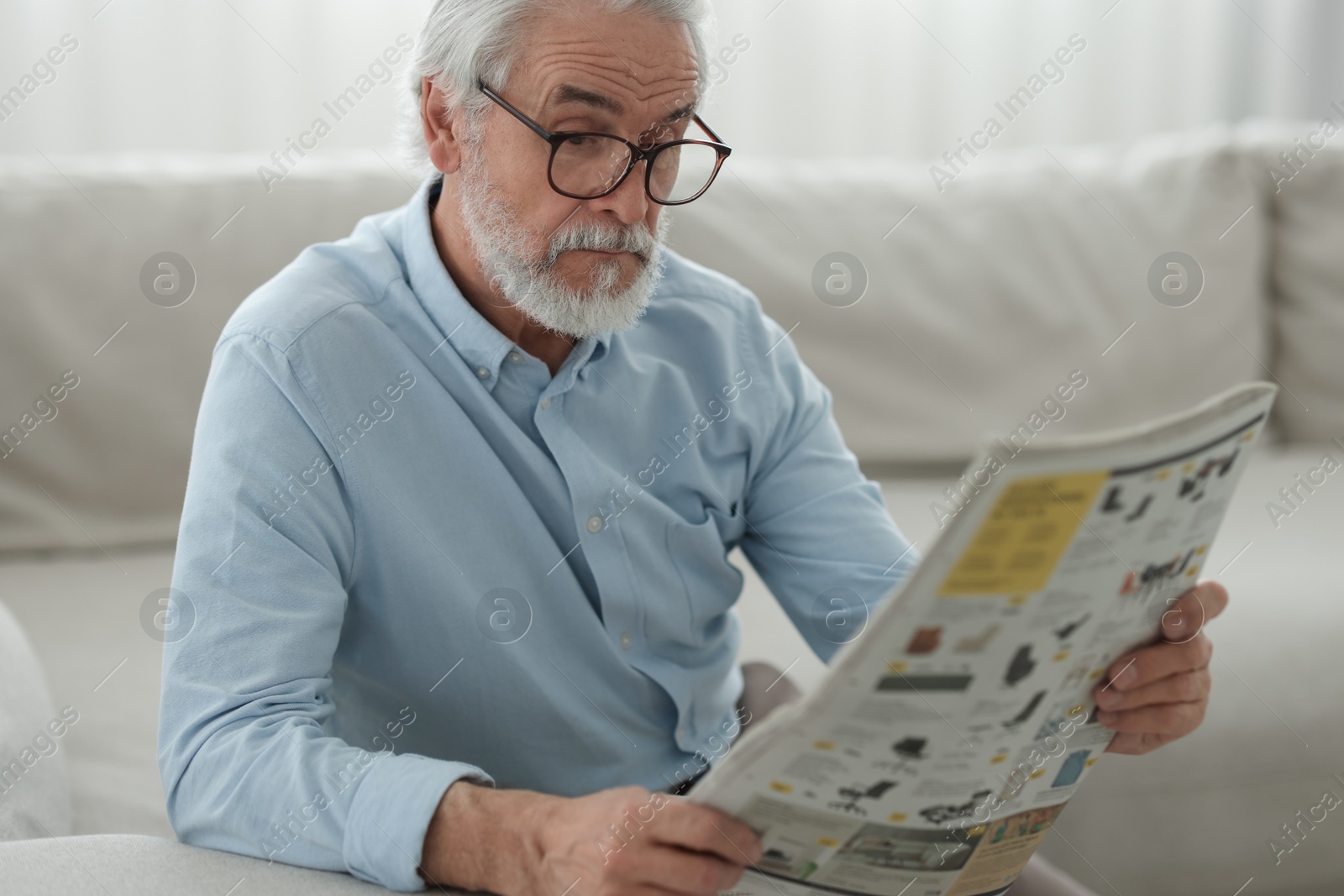 Photo of Portrait of grandpa with stylish glasses reading newspaper on sofa indoors