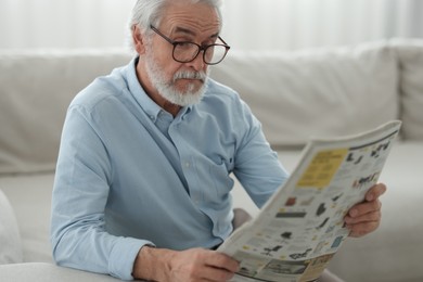 Portrait of grandpa with stylish glasses reading newspaper on sofa indoors