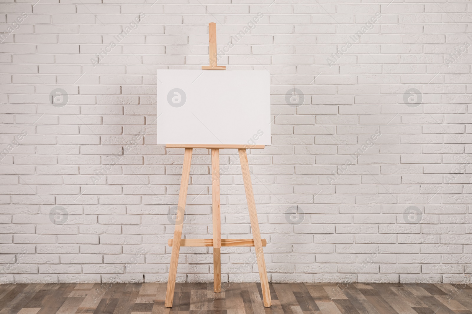 Photo of Wooden easel with blank canvas near white brick wall