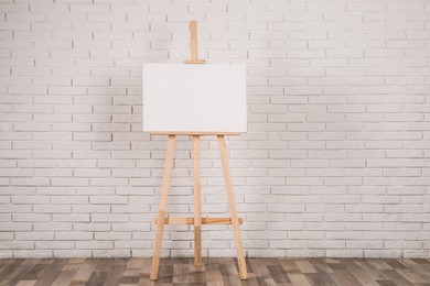 Photo of Wooden easel with blank canvas near white brick wall