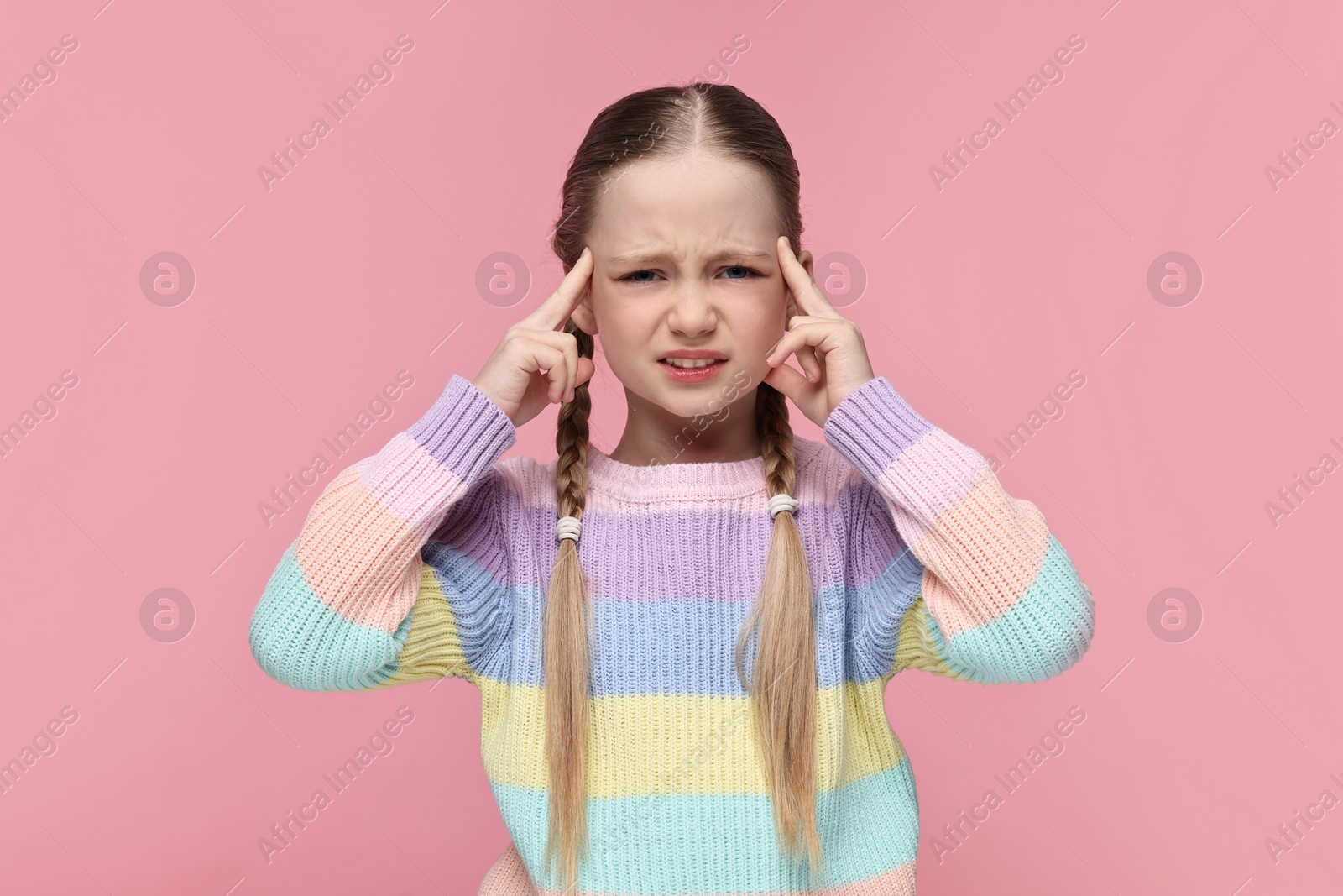 Photo of Little girl suffering from headache on pink background