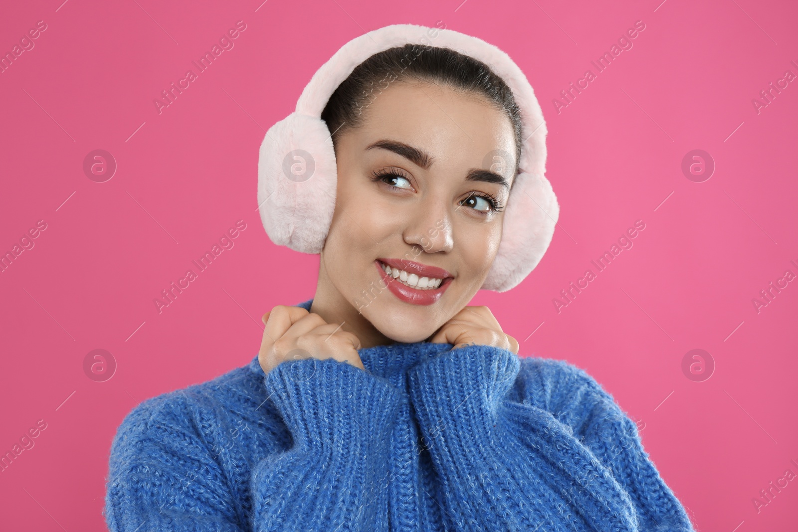 Photo of Beautiful young woman wearing earmuffs on pink background