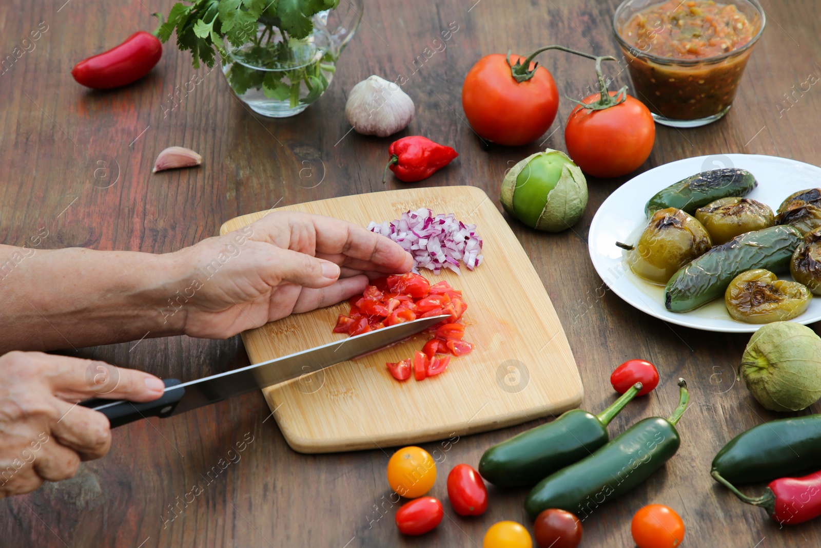 Photo of Woman cutting tomato for salsa sauce at wooden table, closeup