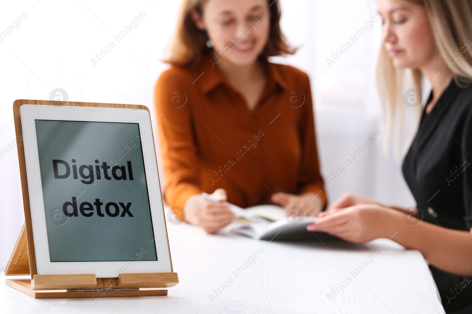 Photo of Women working at table in office, focus on tablet with phrase DIGITAL DETOX