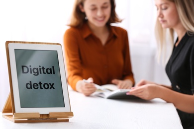 Women working at table in office, focus on tablet with phrase DIGITAL DETOX