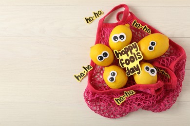 Photo of Mesh bag with lemons and words Happy Fool's Day on wooden table, flat lay. Space for text