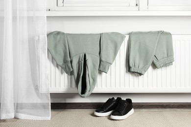 Photo of Heating radiator with clothes and shoes in room