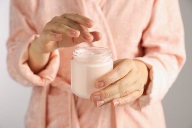 Woman holding jar of hand cream on grey background, closeup