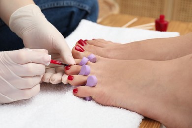 Pedicurist painting client`s toenails with red polish in beauty salon, closeup