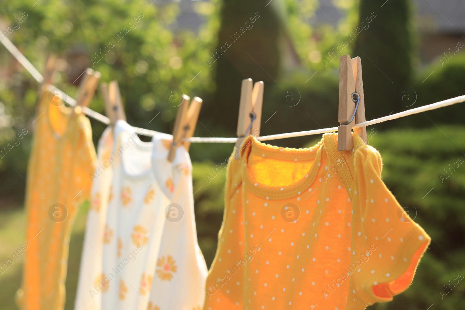 Photo of Clean baby onesies hanging on washing line in garden, closeup. Drying clothes