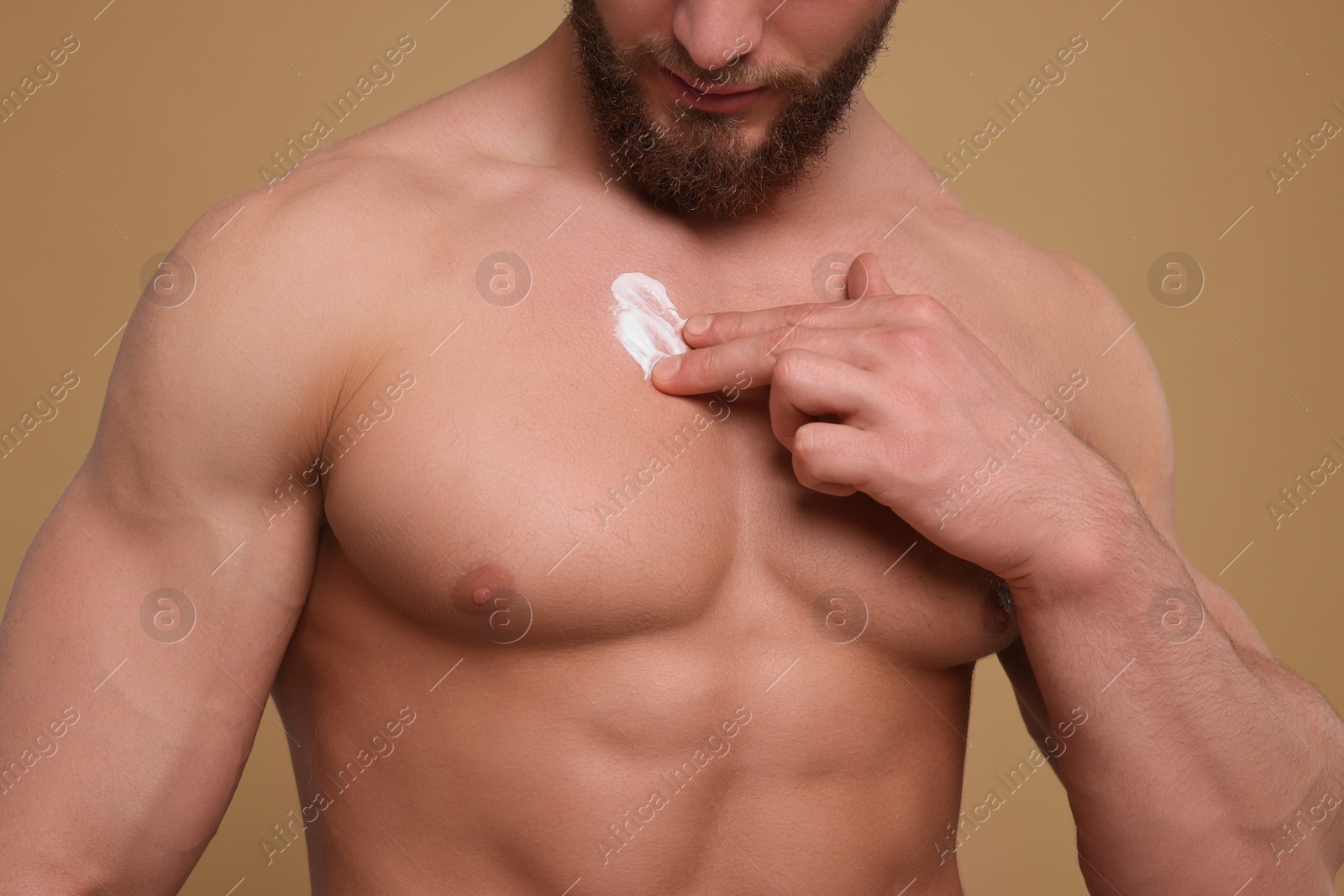 Photo of Man applying body cream onto his chest on pale brown background, closeup