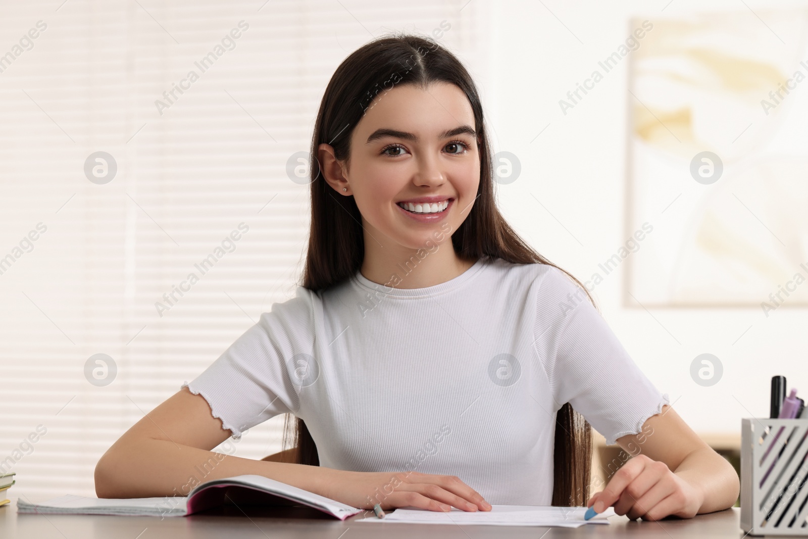 Photo of Teenage girl erasing mistake in her notebook at wooden desk indoors