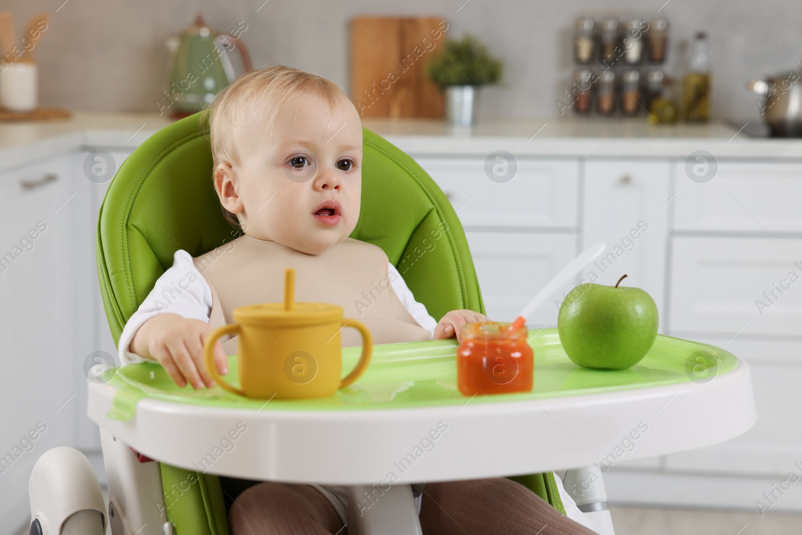 Photo of Cute little baby with healthy food in high chair at home