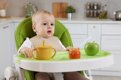 Cute little baby with healthy food in high chair at home