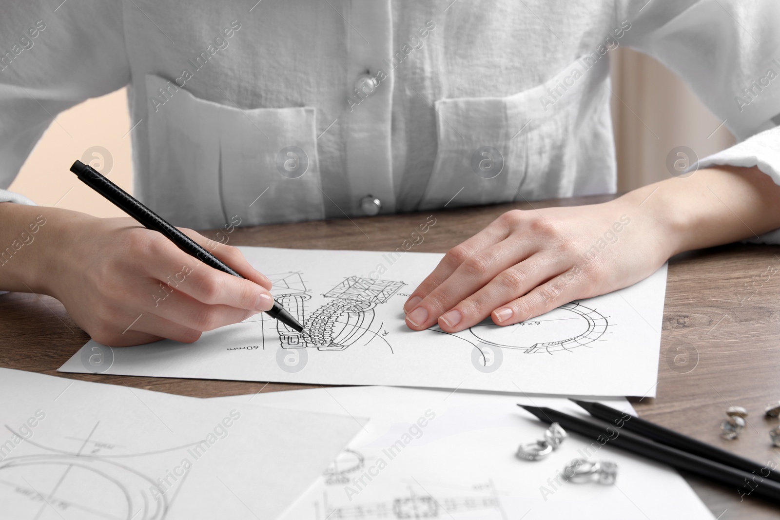 Photo of Jeweler drawing sketch of elegant earrings at wooden table, closeup