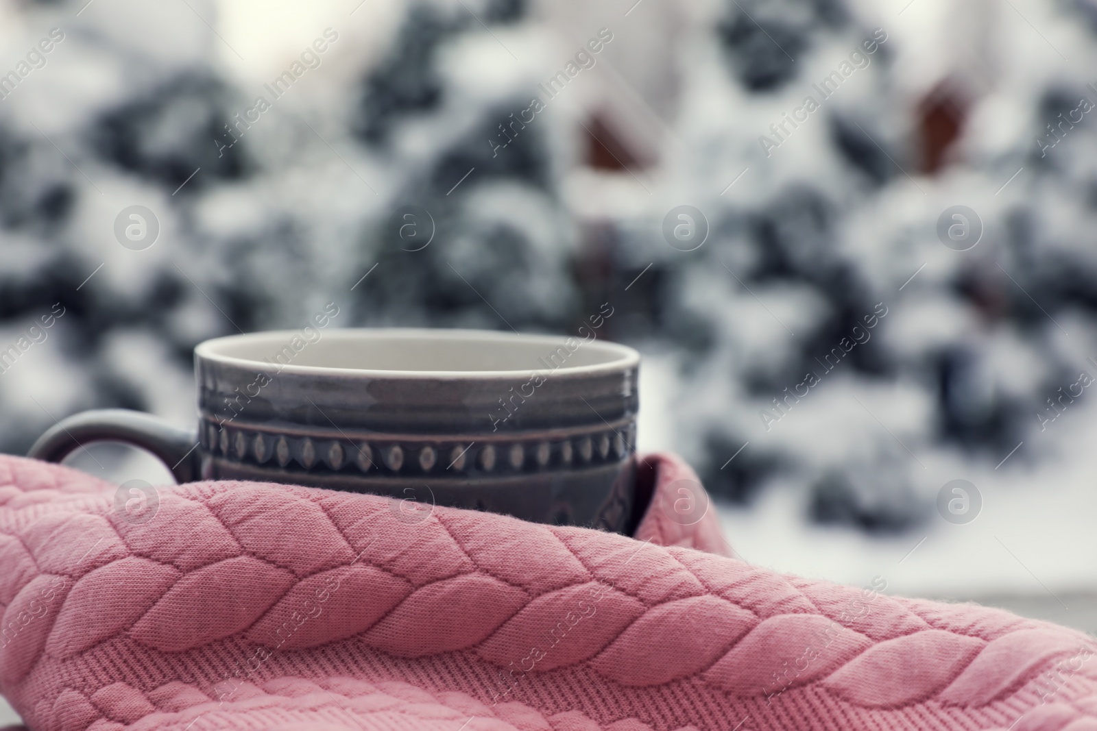 Photo of Winter morning. Cup with hot drink wrapped in pink sweater outdoors, closeup. Space for text