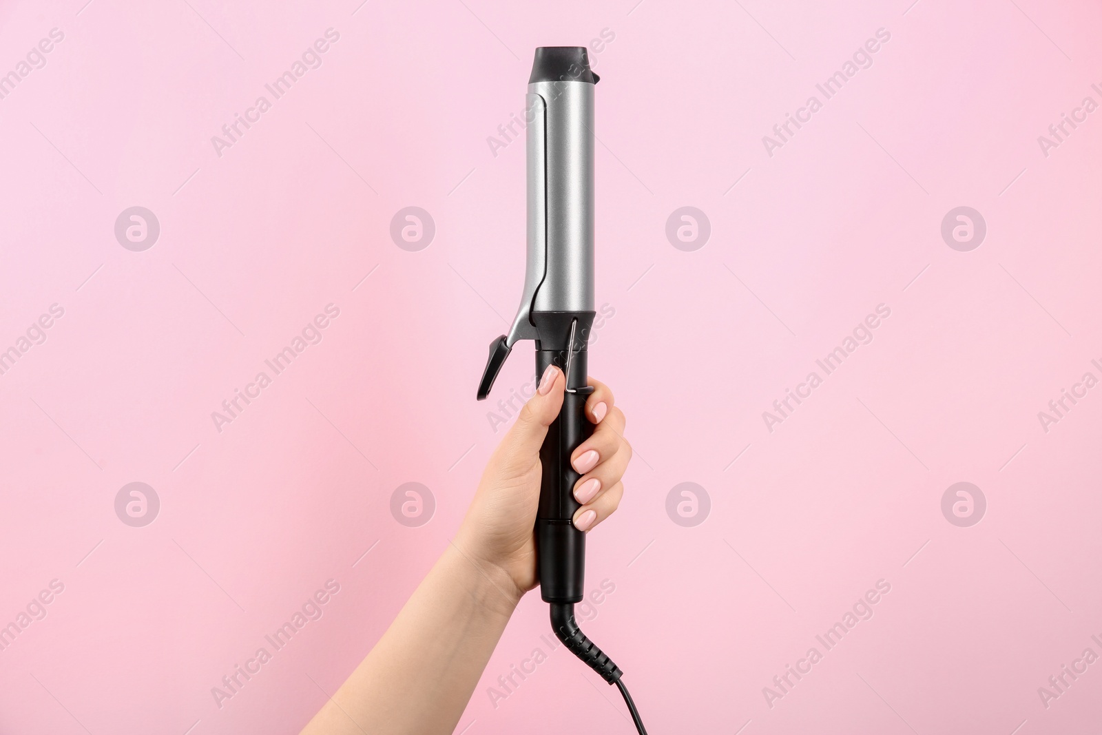 Photo of Hair styling appliance. Woman holding curling iron on pink background, closeup