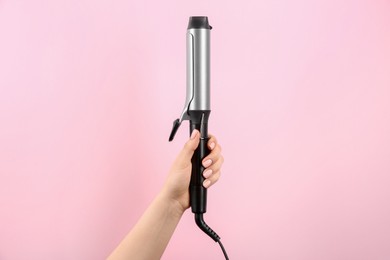 Photo of Hair styling appliance. Woman holding curling iron on pink background, closeup