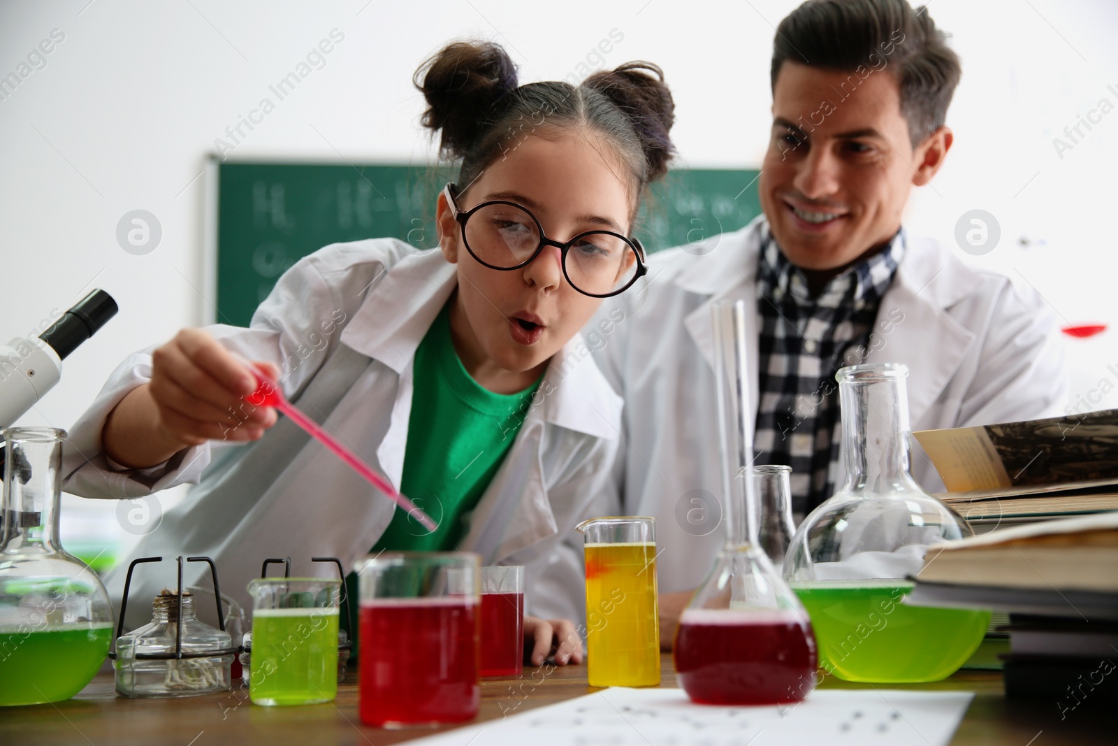 Photo of Teacher with pupil making experiment at table in chemistry class