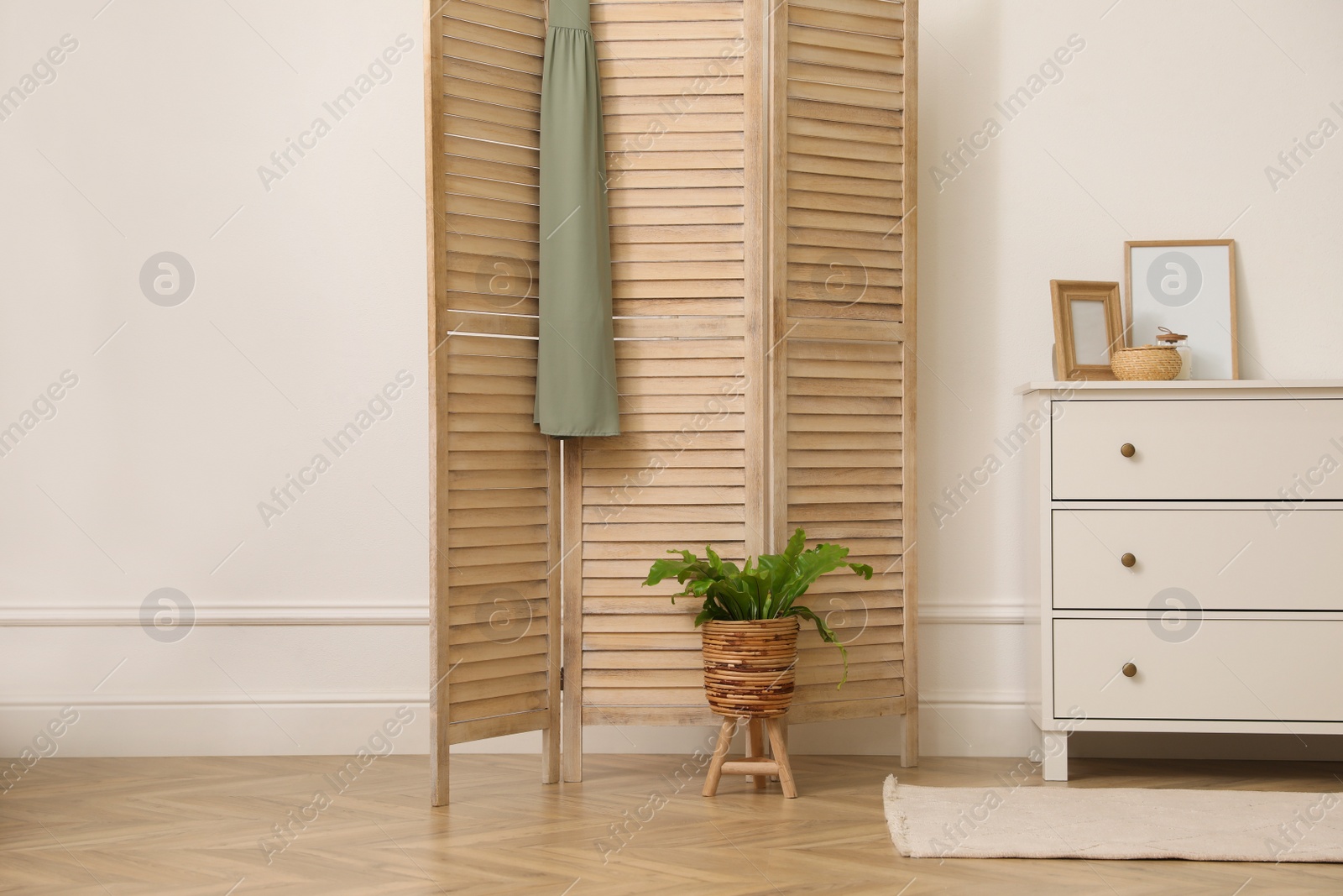 Photo of Stylish room with wooden folding screen and chest of drawers near white wall. Interior design