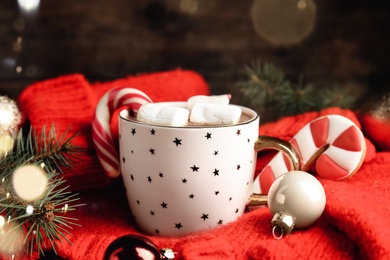 Photo of Cup of tasty cocoa with marshmallows, candy cane and Christmas decor on knitted sweater