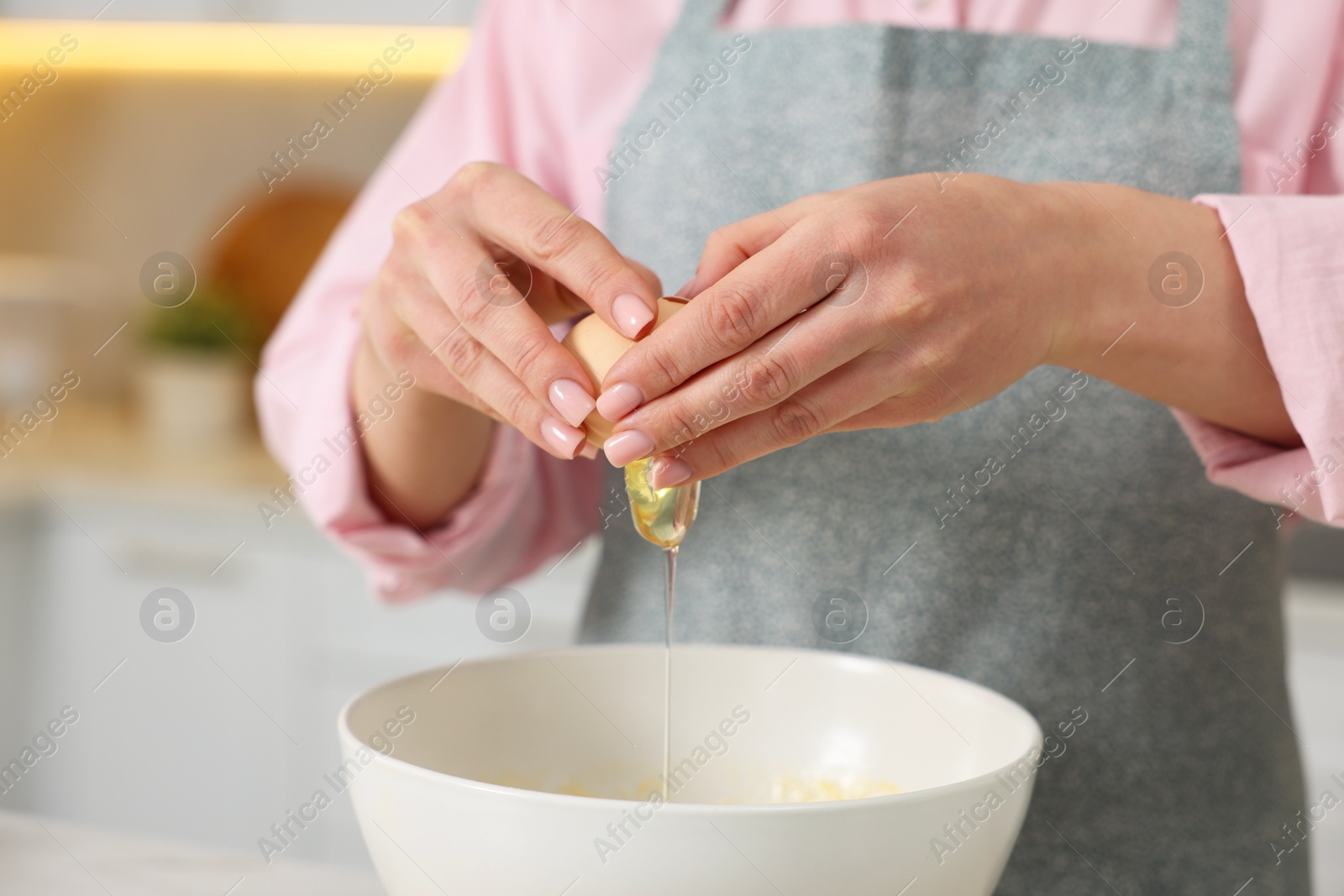 Photo of Making bread. Woman putting raw egg into bowl at white table in kitchen, closeup