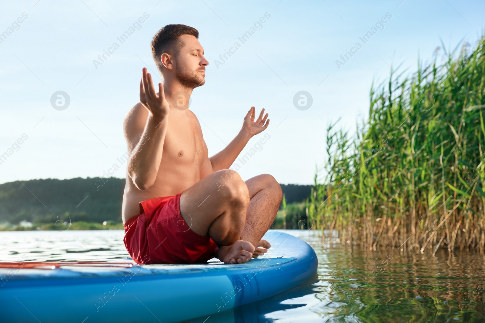 Photo of Man meditating on light blue SUP board on river at sunset