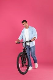 Handsome young man with modern bicycle on pink background